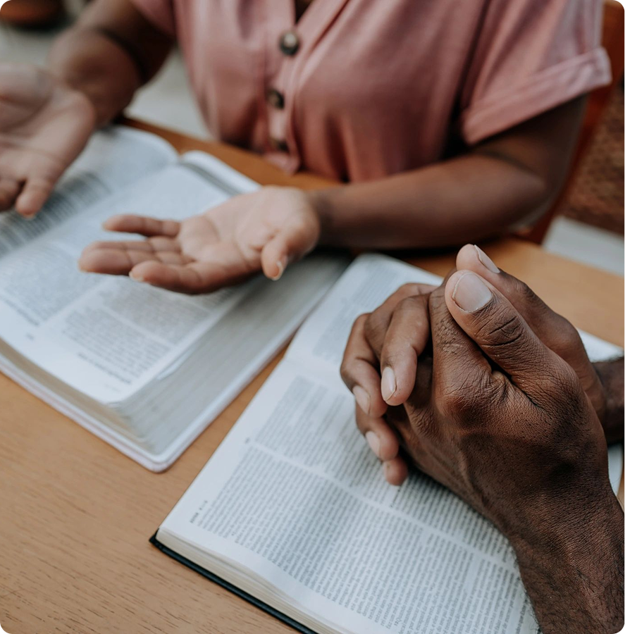 Hands praying over open Bible books.